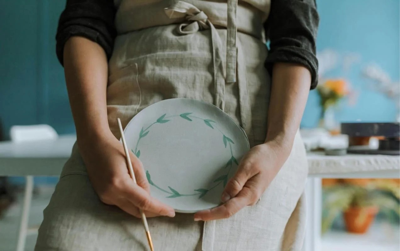 woman holding a plate that she's painted and wearing an apron