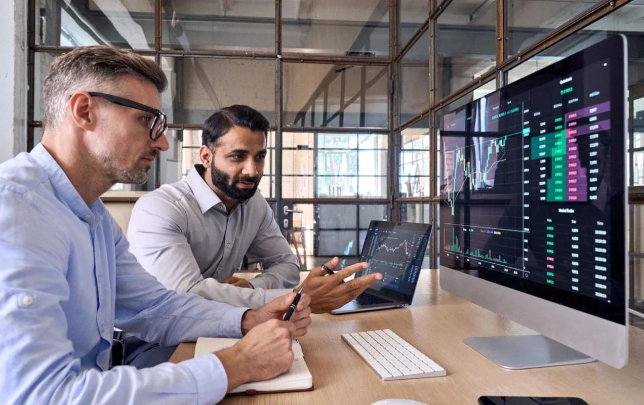 two men reviewing charts and graphs on a desktop computer