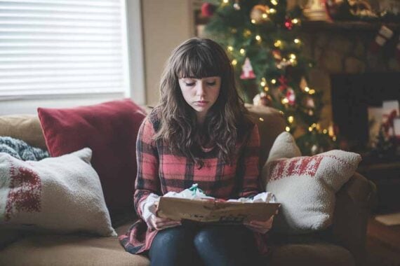 Photo of a teenage female looking sad in front of a Christmas tree