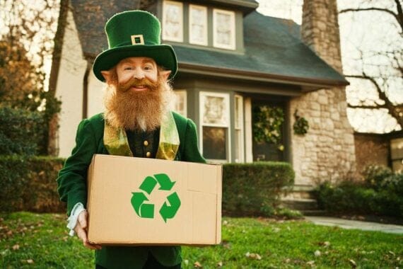 Male in a green leprecon costume holding a box with a "sustainability" emblem