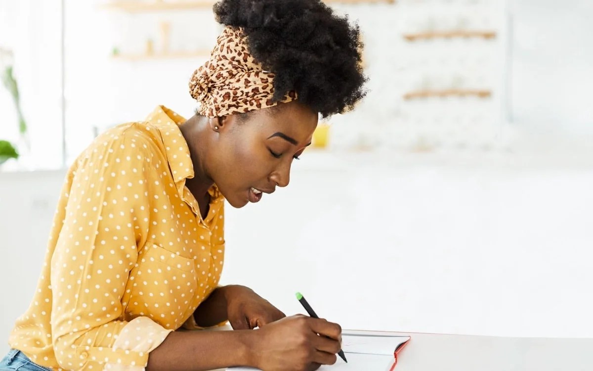 woman in a yellow polka dot shirt writing in a journal